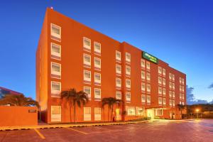 un grand bâtiment oranger avec des palmiers dans un parking dans l'établissement City Express Junior by Marriott Ciudad del Carmen, à Ciudad del Carmen