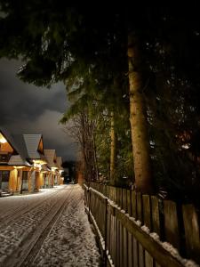 eine verschneite Straße in der Nacht mit einem Zaun und Bäumen in der Unterkunft Osada Zbójnicka Turnia in Kościelisko