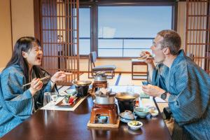 Ein Mann und eine Frau sitzen am Tisch und essen Essen. in der Unterkunft Awakan in Sumoto
