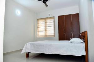 a white bedroom with a bed and a window at Krishna Dhwani Apartments in Tellicherry