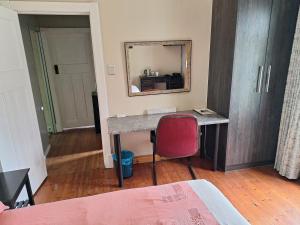 a bedroom with a desk with a red chair and a mirror at Rooster Room in Boksburg