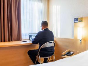 ibis Lyon Gare Part Dieu في ليون: رجل يجلس على كرسي يستخدم الكمبيوتر المحمول في غرفة في الفندق