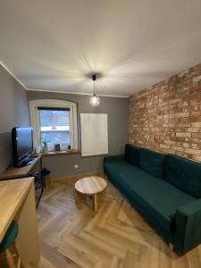a living room with a green couch and a brick wall at Apartament Rose Valley Dwa Zero in Szczytna