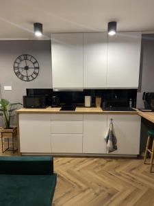 a kitchen with white cabinets and a clock on the wall at Apartament Rose Valley Dwa Zero in Szczytna