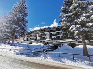 a building covered in snow next to a street at La Finestra sul Brenta con POSTO AUTO PRIVATO AL CENTRO di MAD di Campiglio CIPAT O22233-AT-O13262 in Folgarida