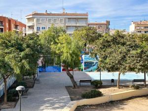Solecito Santa Pola. Relax and beach 4 min away في سانتا بولا: حديقة بها مقاعد وأشجار أمام مبنى