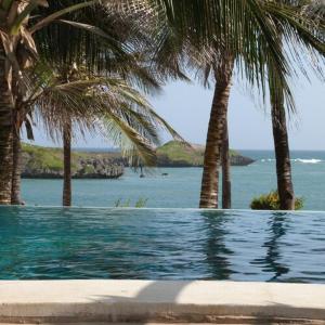 a swimming pool with palm trees and the ocean at Aquarius Club in Watamu
