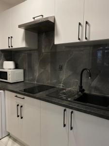 a kitchen with white cabinets and a sink and a microwave at Apartament Pogodno in Szczecin