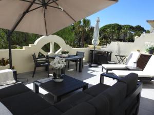 a patio with couches and tables and an umbrella at Beautiful 2-Bed Villa in Quinta do Lago with Pool in Quinta do Lago
