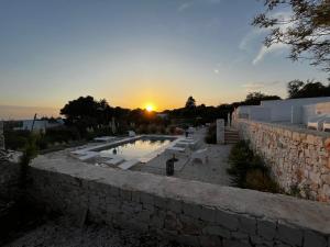a sunset over a stone wall with a swimming pool at Villa Ada-Trulli Puglia in Martina Franca