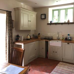 uma cozinha com armários brancos, um lavatório e uma mesa em Luxury Exmoor Barn conversion with Sauna em Exford