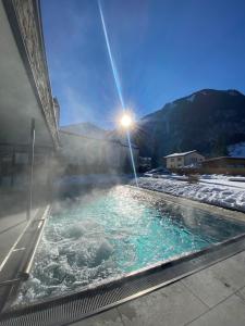 a hot tub with snow on the ground with the sun shining at Hotel Römerhof in Fusch an der Glocknerstraße