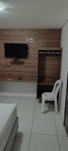a bedroom with a tv and a white chair in a room at Pousada Gaby in Salgueiro