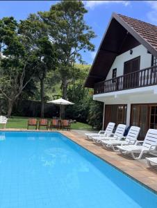 uma piscina com cadeiras e uma casa em Jardim Secreto - Itaipava em Itaipava