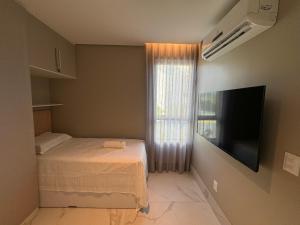 een kleine slaapkamer met een bed en een flatscreen-tv bij Flat+deck ao lado da igrejinha in Praia dos Carneiros
