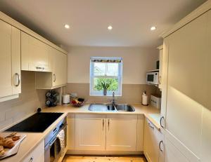 een keuken met witte kasten, een wastafel en een raam bij Cosy Cotswold Home - Jacobs Cottage in Cirencester