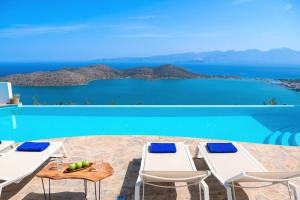 a pool with white chairs and a view of the ocean at Luxury Villa Orea, Elounda (owner's listing) in Epáno Eloúnda