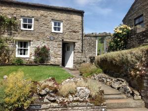 a stone house with a white door and a yard at Cissy's Cottage in Hawes