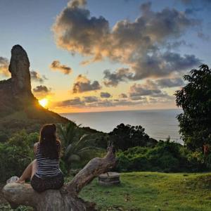 a woman sitting on a tree stump watching the sunset at Casa Beco do Céu in Fernando de Noronha
