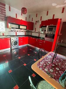 une cuisine avec des placards rouges, une table et un lave-linge dans l'établissement Villa spacieuse 200 m à la plage, à Zarzis
