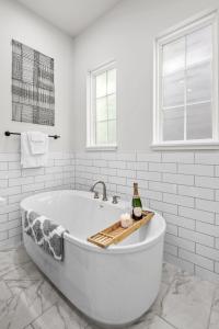 a bath tub in a white bathroom with a bottle of wine at Lux Living - East Downtown Rooftop with King Suite & Private Chef in Houston
