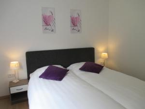 ein Schlafzimmer mit einem weißen Bett mit zwei lila Kissen in der Unterkunft Ferienhaus Rheiderland in Ditzumerverlaat