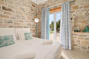 a bedroom with a white bed and a stone wall at Aphrodite's Luxury Pearls 2 in Pitsidia