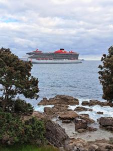 a cruise ship in the ocean with rocks in the foreground at Sunbrae Beach luxury in Mount Maunganui