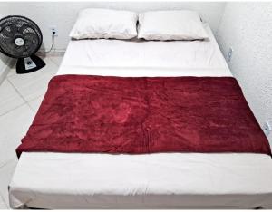 a bed with a red blanket on it with a fan at Mini Casa Aconchegante in Saquarema