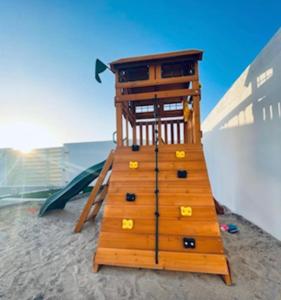 una estructura de juegos de madera en la playa con un parque infantil en Al Saleh Chalet en Al Ashkharah