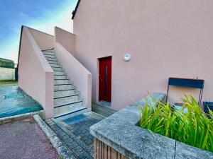 różowy dom z czerwonymi drzwiami i schodami w obiekcie Appartement calme à 3 min de la plage avec terrasse, parking et WIFI - FR-1-714-1 w mieście Clohars-Carnoët