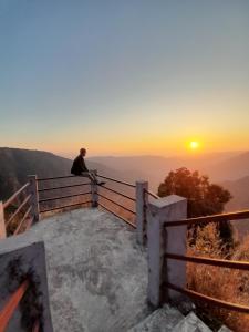 a man sitting on a fence watching the sunset at Living Roots Lodge in Cherrapunji