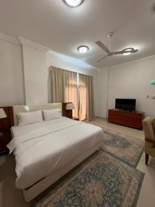 um quarto com uma grande cama branca e uma televisão em بيت السلطانة للأجنحة الفندقية em Salalah