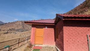 a red and orange building with a hill in the background at Dhauladhar Woodhouse in Malotha