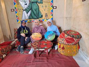 three women sitting on chairs in a room with a painting at Queen House in Aswan