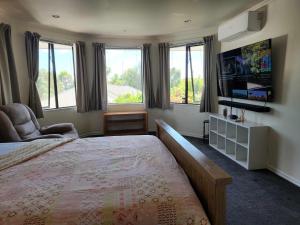 een slaapkamer met een bed, een tv en ramen bij Accommodations Homestay in Rototuna, Hamilton in Hamilton