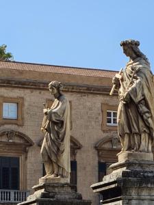 Deux statues de deux personnes devant un bâtiment dans l'établissement La Loggia dei Re, à Palerme