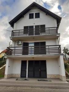 a white house with black shutters and a balcony at Balatonberényi Vendégház in Balatonberény