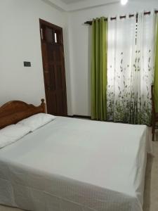 a bedroom with a white bed and green curtains at White's vila in Matara