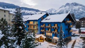 a blue building with snowy mountains in the background at Hotel Baita Clementi in Bormio