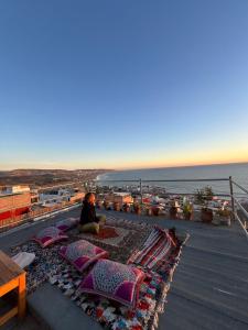 a woman sitting on top of a roof with pillows at Hostel blue house Taghazout in Taghazout