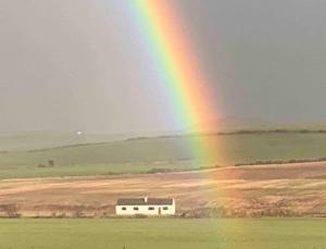 a rainbow in the sky over a field with a building at Inishroel Cottage in Campbeltown