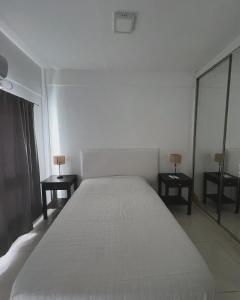 a white bedroom with a large bed and two tables at Departamento Moritan in Posadas