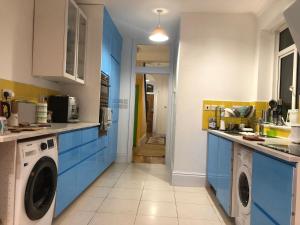a kitchen with blue cabinets and a washer and dryer at Rosie Cosy House Cricklewood in London