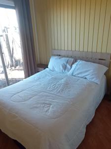 a bed with white sheets and pillows next to a window at Cabaña Curanipe Playa in Curanipe