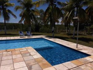a swimming pool with two chairs and palm trees at Paraiso Pasargada in Japaratinga