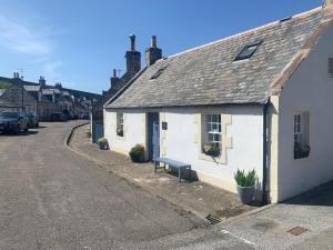 a white building with a bench next to a street at Zen Cottage Seatown Cullen in Cullen
