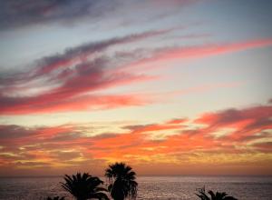 zachód słońca nad oceanem z palmami na pierwszym planie w obiekcie Casa Bella Vista frente al mar y piscina natural. w mieście Charco del Palo