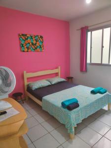 a bedroom with a bed and a pink wall at Aquarela Suítes in Piúma