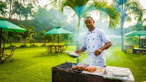 Een man kookt vlees op een grill. bij Roma Stays - Magnificent 4BR at Sunset Paradise Shanzu with a Swimming Pool in Mombasa